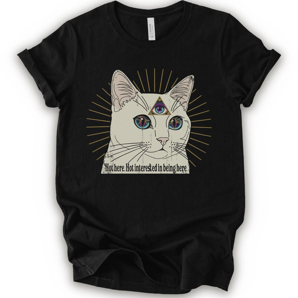 A black short-sleeve crewneck t-shirt featuring a graphic of a white cat with a third eye and gold sunburst rays, with the text 'Not here. Not interested in being here.