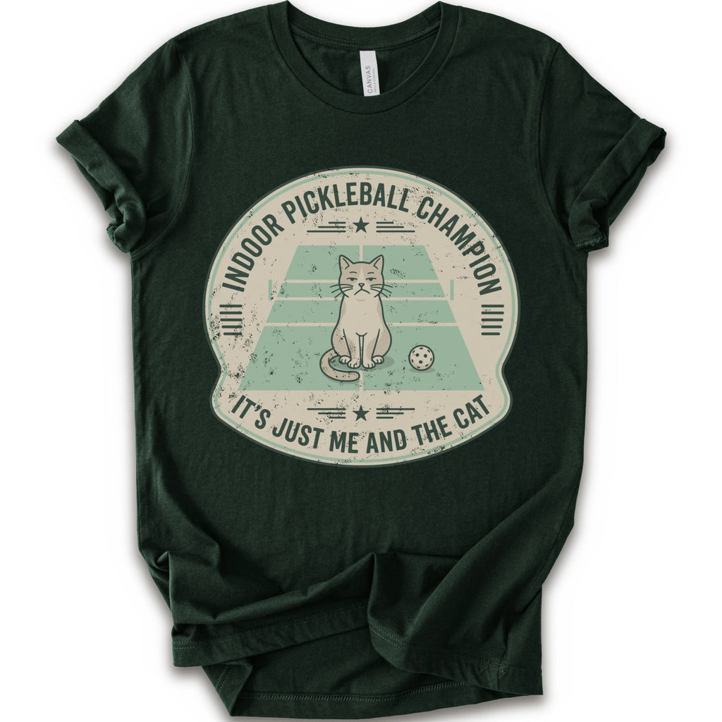 A forest short-sleeve crewneck t-shirt with a distressed circular graphic on the front, features a cartoon cat playing pickleball on a court, with the text 'INDOOR PICKLEBALL CHAMPION' and 'IT'S JUST ME AND THE CAT'.