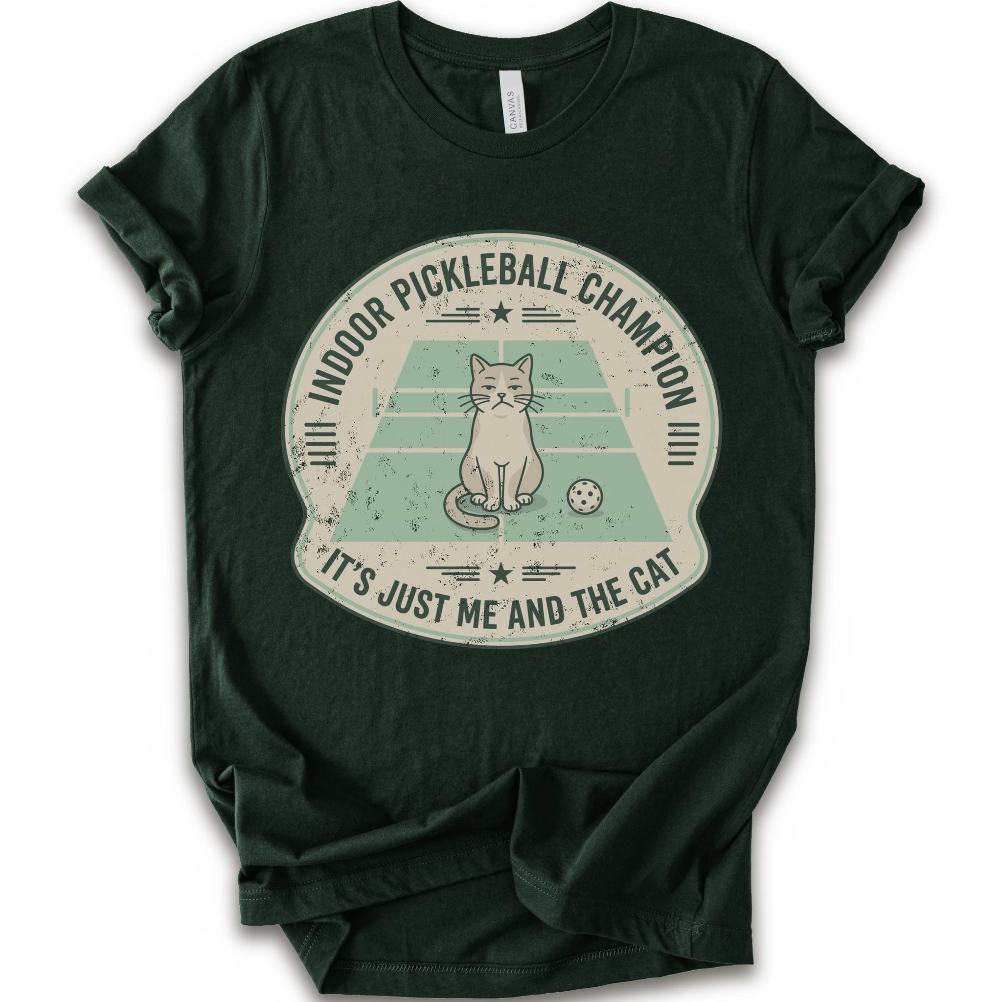 A forest short-sleeve crewneck t-shirt with a distressed circular graphic on the front, features a cartoon cat playing pickleball on a court, with the text 'INDOOR PICKLEBALL CHAMPION' and 'IT'S JUST ME AND THE CAT'.