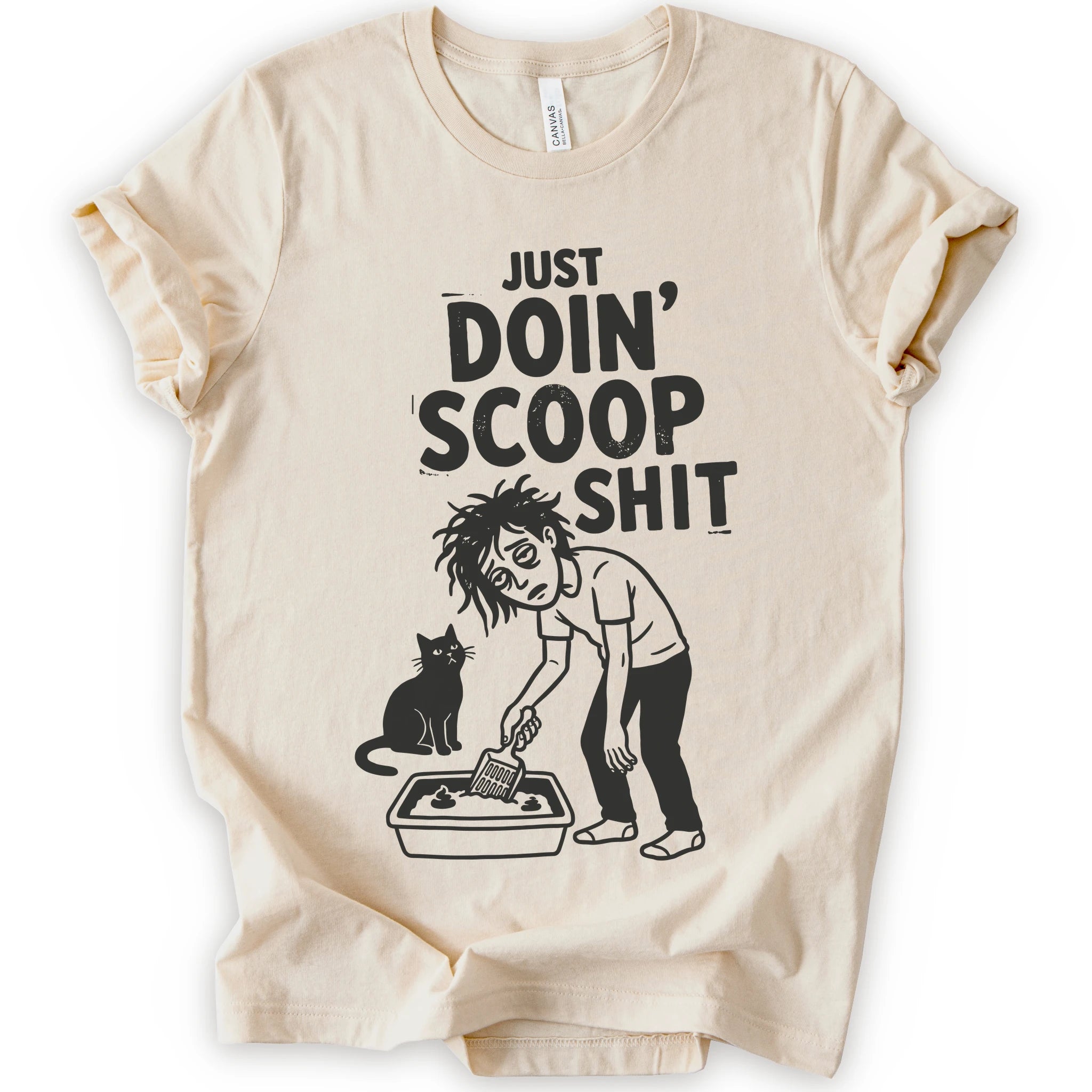 A natural short-sleeve crewneck t-shirt featuring a graphic with 
“Just Doin’ Scoop Shit” text above a tired cat owner cleaning a litter box beside a seated cat