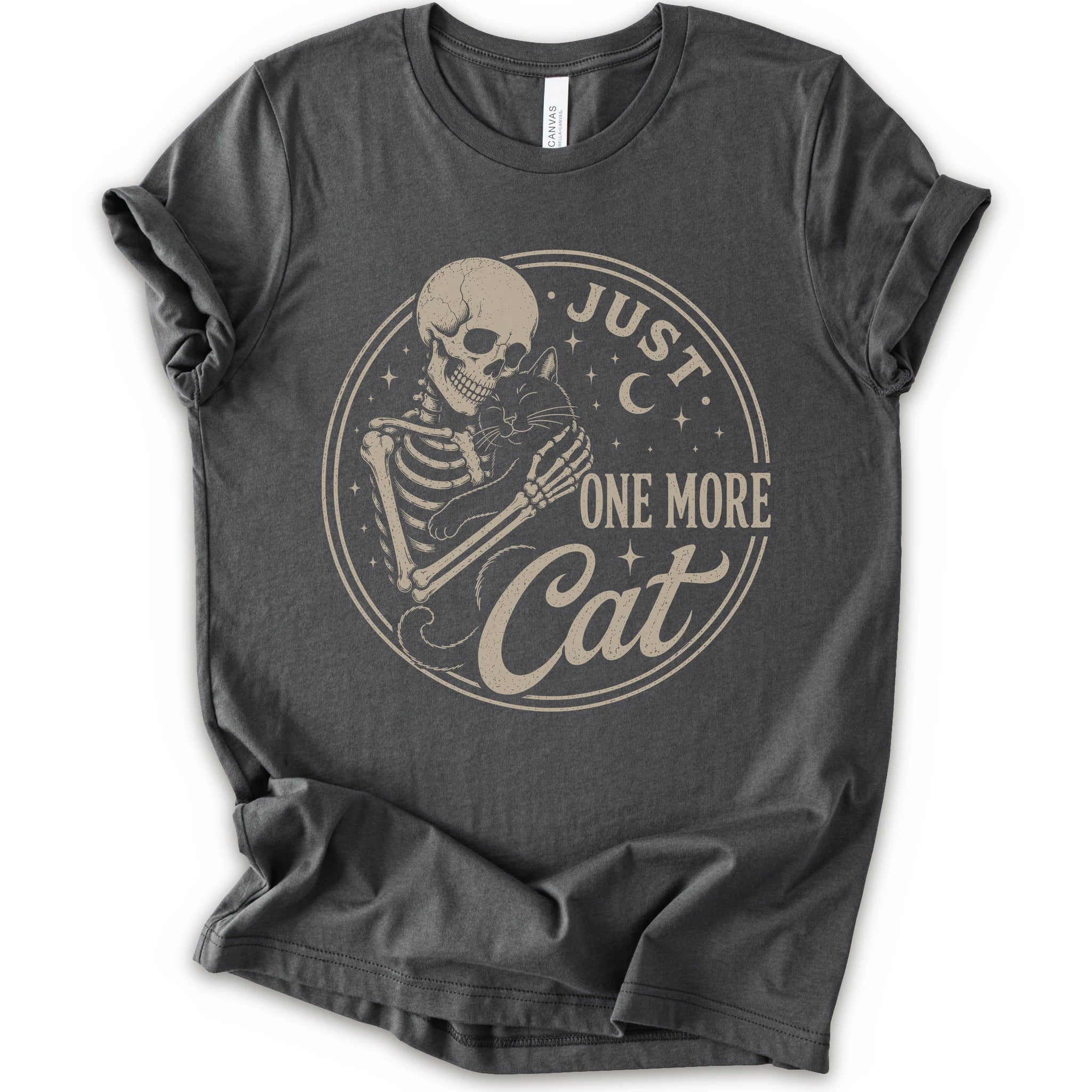 A asphalt short-sleeve crewneck t-shirt with a distressed beige graphic of a skeleton holding a cat, surrounded by the text 'JUST ONE MORE Cat' inside a circular design.