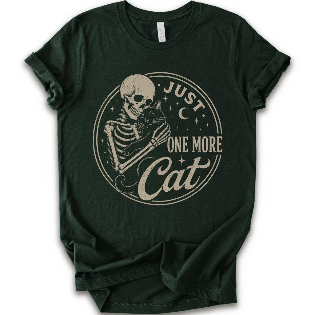 A dark forest green short-sleeve t-shirt with a vintage-style beige graphic on the front showing a skeleton holding a cat, with the text 'JUST ONE MORE Cat'.
