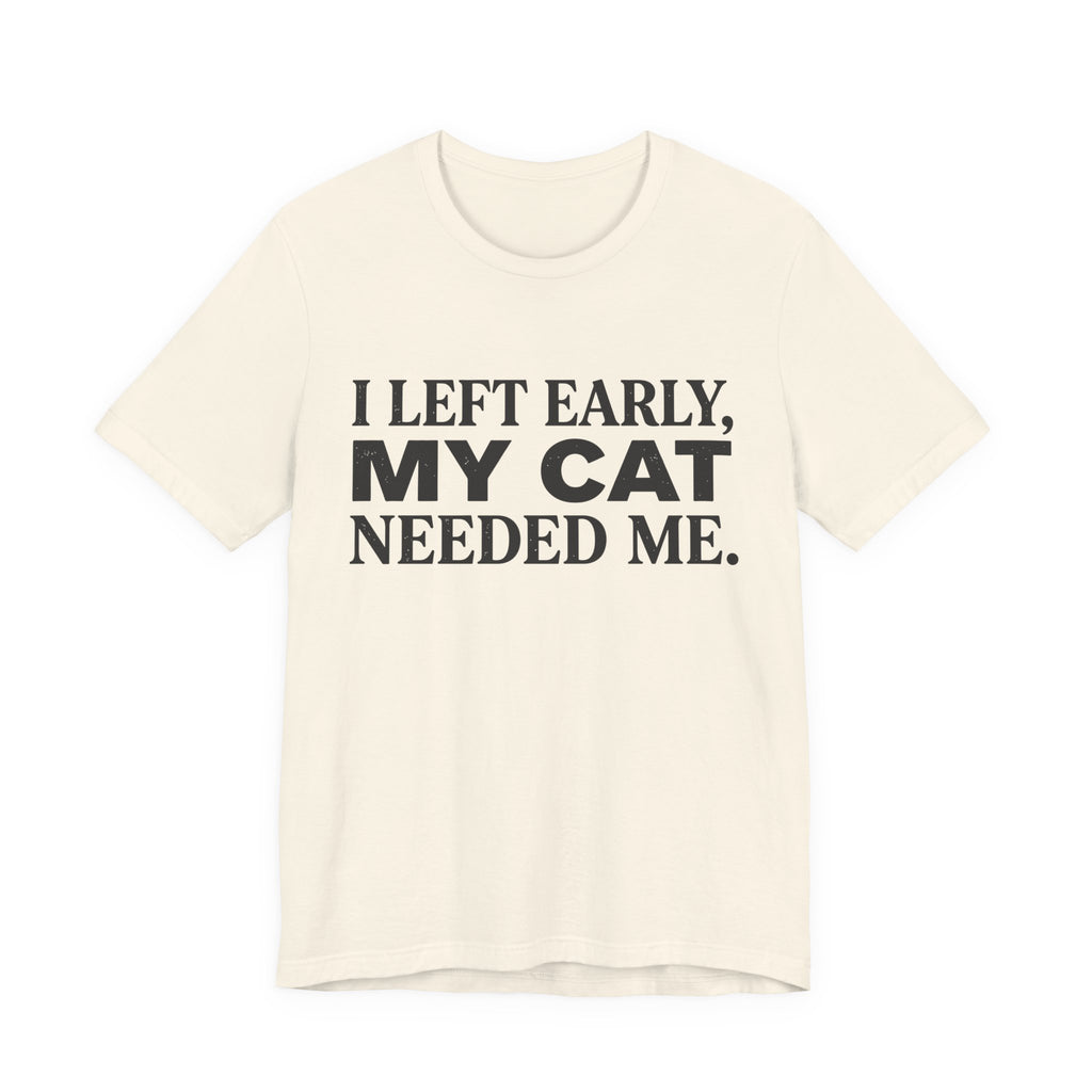 A natural short-sleeve crewneck t-shirt featuring a graphic with black text reading “I Left Early, My Cat Needed Me” arranged in three bold lines
