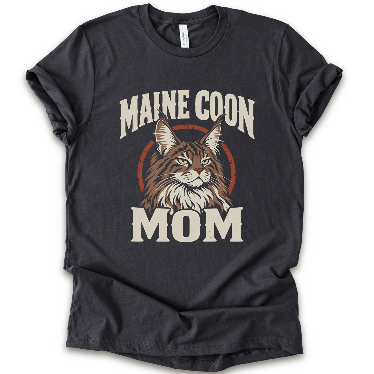 A dark grey short-sleeve crewneck t-shirt featuring a graphic print of a Maine Coon cat with the text 'MAINE COON MOM' in distressed cream lettering.