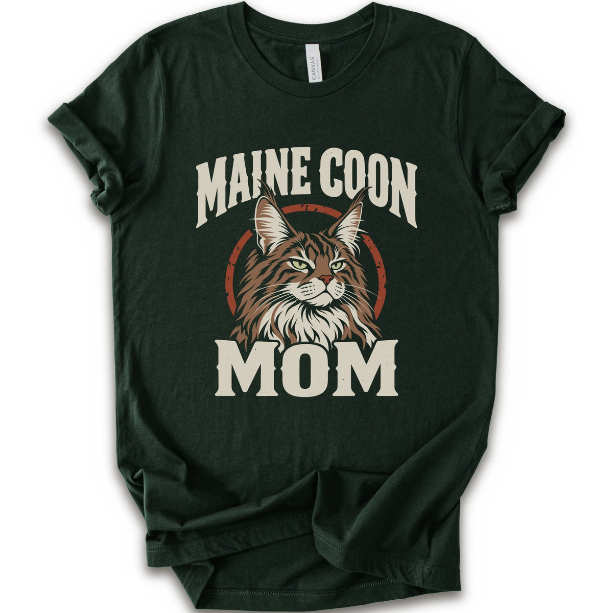 A forest short-sleeve crewneck t-shirt featuring a graphic print of a Maine Coon cat with the text 'MAINE COON MOM' in distressed cream lettering.