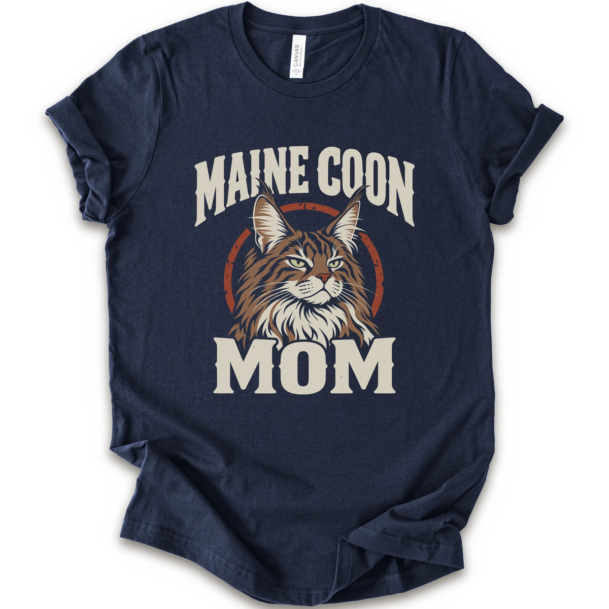A navy short-sleeve crewneck t-shirt featuring a graphic print of a Maine Coon cat with the text 'MAINE COON MOM' in distressed cream lettering.