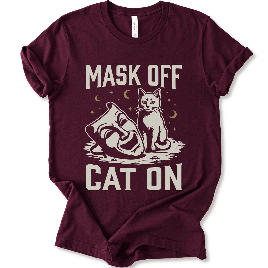 A maroon short-sleeve crewneck t-shirt with a white graphic with gold moons and stars of a cat with a mask surrounded by the text 'MASK OFF' and 'CAT ON'.