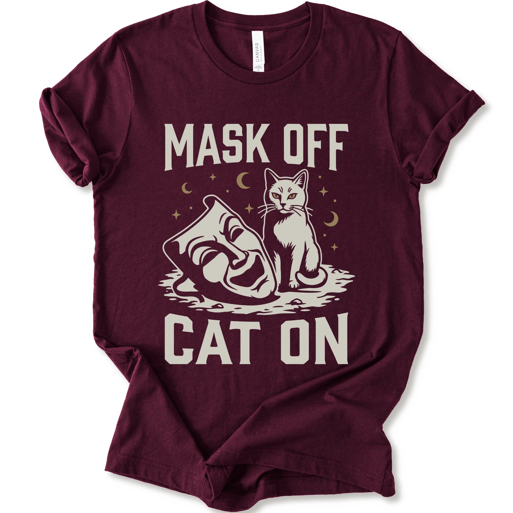 A maroon short-sleeve crewneck t-shirt with a white graphic with gold moons and stars of a cat with a mask surrounded by the text 'MASK OFF' and 'CAT ON'.