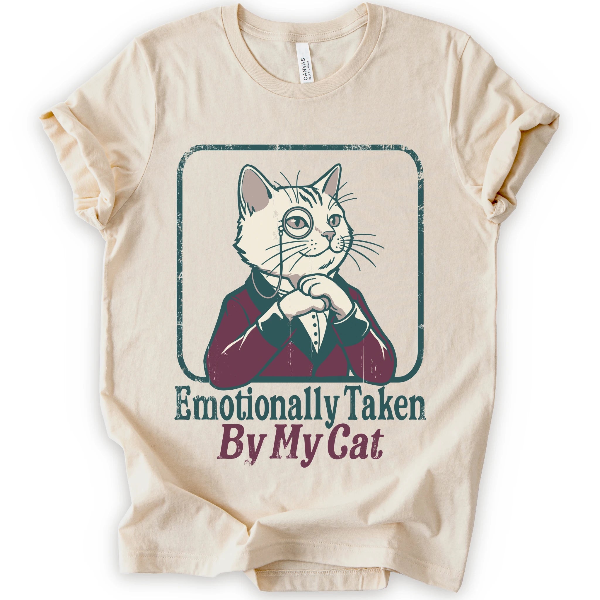 A natural short-sleeve t-shirt with a graphic of a cat dressed in a burgundy suit and top hat inside a distressed border, with the text 'Emotionally Taken By My Cat' printed below.