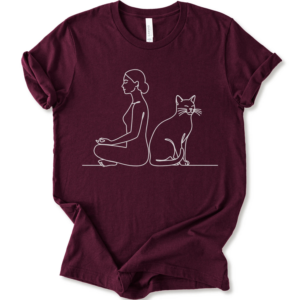 A maroon short-sleeve crewneck t-shirt with a minimalist white line art graphic of a woman in a meditation pose next to a cat.