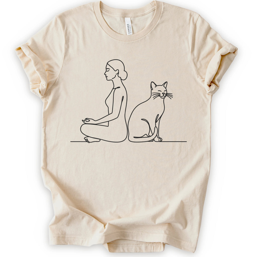 A natural short-sleeve crewneck t-shirt with a minimalist black line art graphic of a woman in a meditation pose next to a cat.