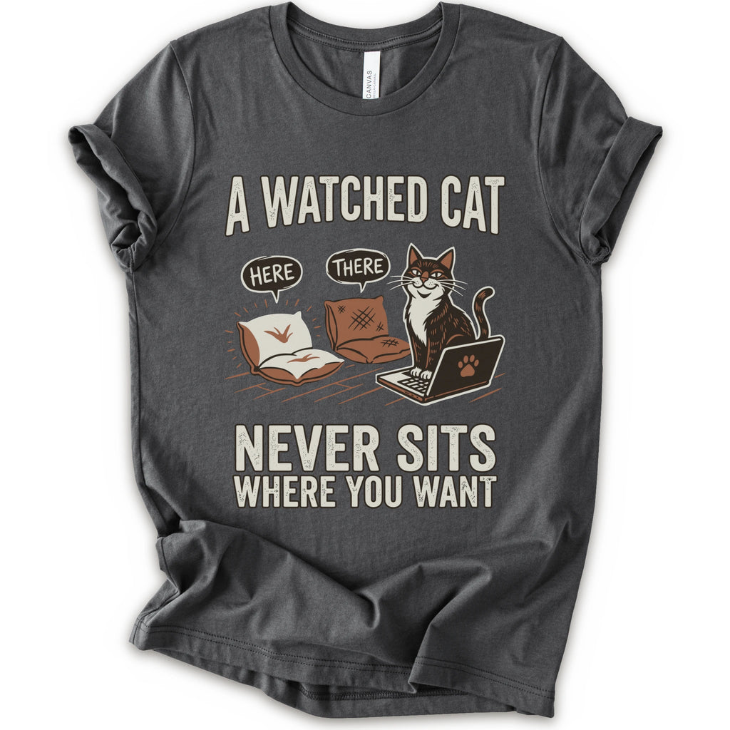 A asphalt  short-sleeve crewneck t-shirt with a humorous graphic print of a cat on a laptop and couch, featuring the text 'A WATCHED CAT NEVER SITS WHERE YOU WANT' and speech bubbles reading 'HERE' and 'THERE'.