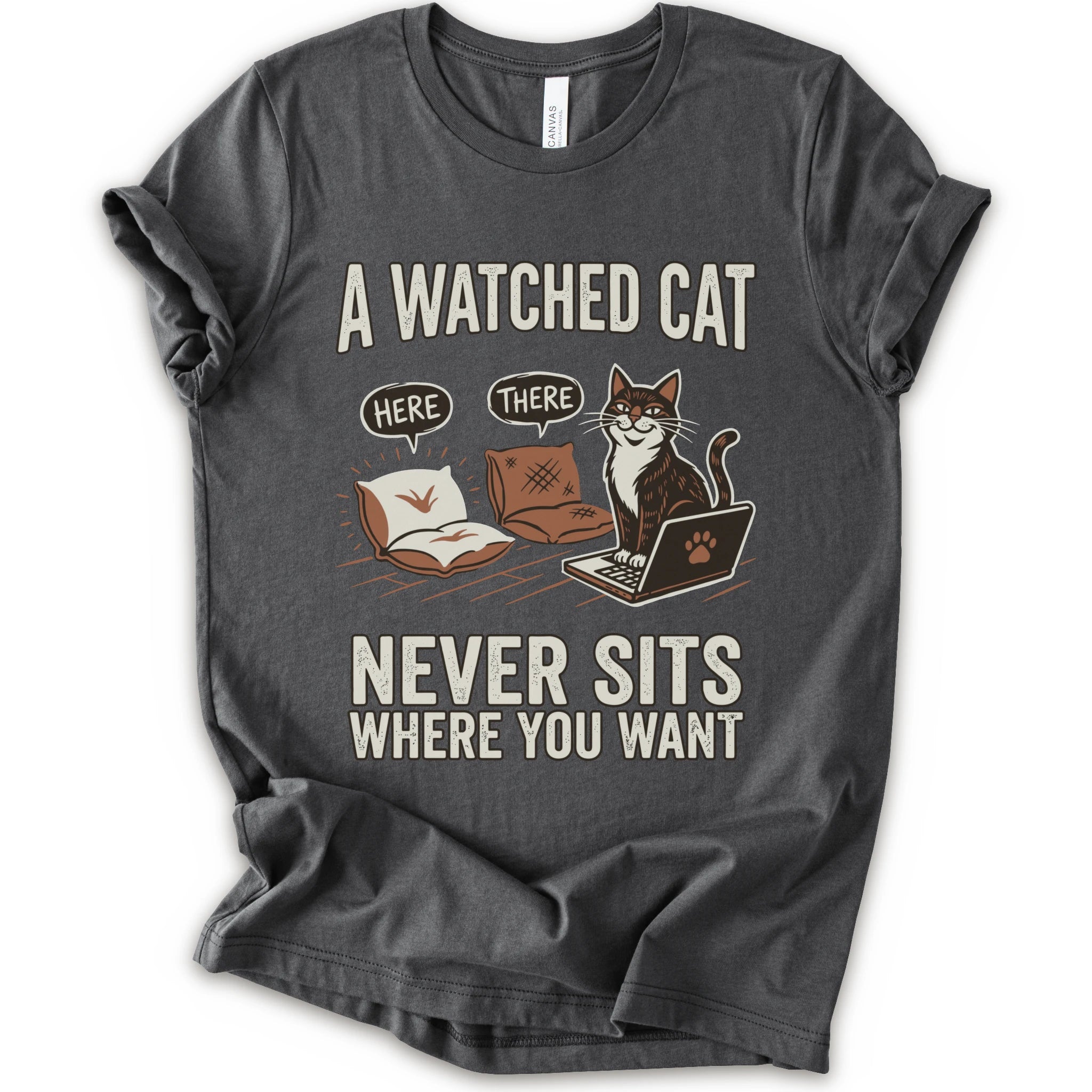 A asphalt  short-sleeve crewneck t-shirt with a humorous graphic print of a cat on a laptop and couch, featuring the text 'A WATCHED CAT NEVER SITS WHERE YOU WANT' and speech bubbles reading 'HERE' and 'THERE'.