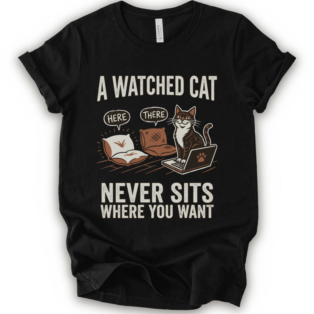 A black short-sleeve crewneck t-shirt with a humorous graphic print of a cat on a laptop and couch, featuring the text 'A WATCHED CAT NEVER SITS WHERE YOU WANT' and speech bubbles reading 'HERE' and 'THERE'.