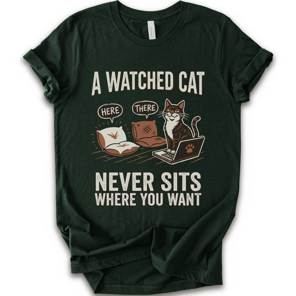A forest short-sleeve crewneck t-shirt with a humorous graphic print of a cat on a laptop and couch, featuring the text 'A WATCHED CAT NEVER SITS WHERE YOU WANT' and speech bubbles reading 'HERE' and 'THERE'.