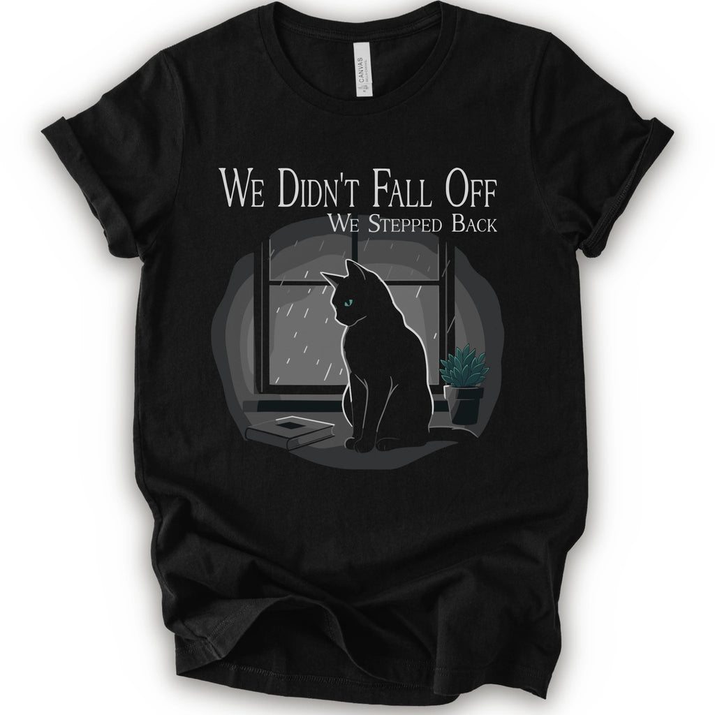 A black short-sleeve crewneck t-shirt with a graphic print of a black cat sitting in front of a window with the text 'WE DIDN'T FALL OFF WE STEPPED BACK'.