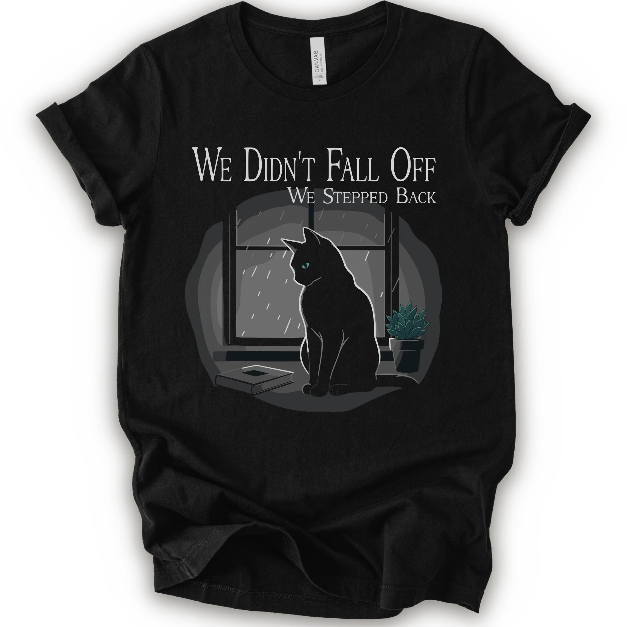 A black short-sleeve crewneck t-shirt with a graphic print of a black cat sitting in front of a window with the text 'WE DIDN'T FALL OFF WE STEPPED BACK'.