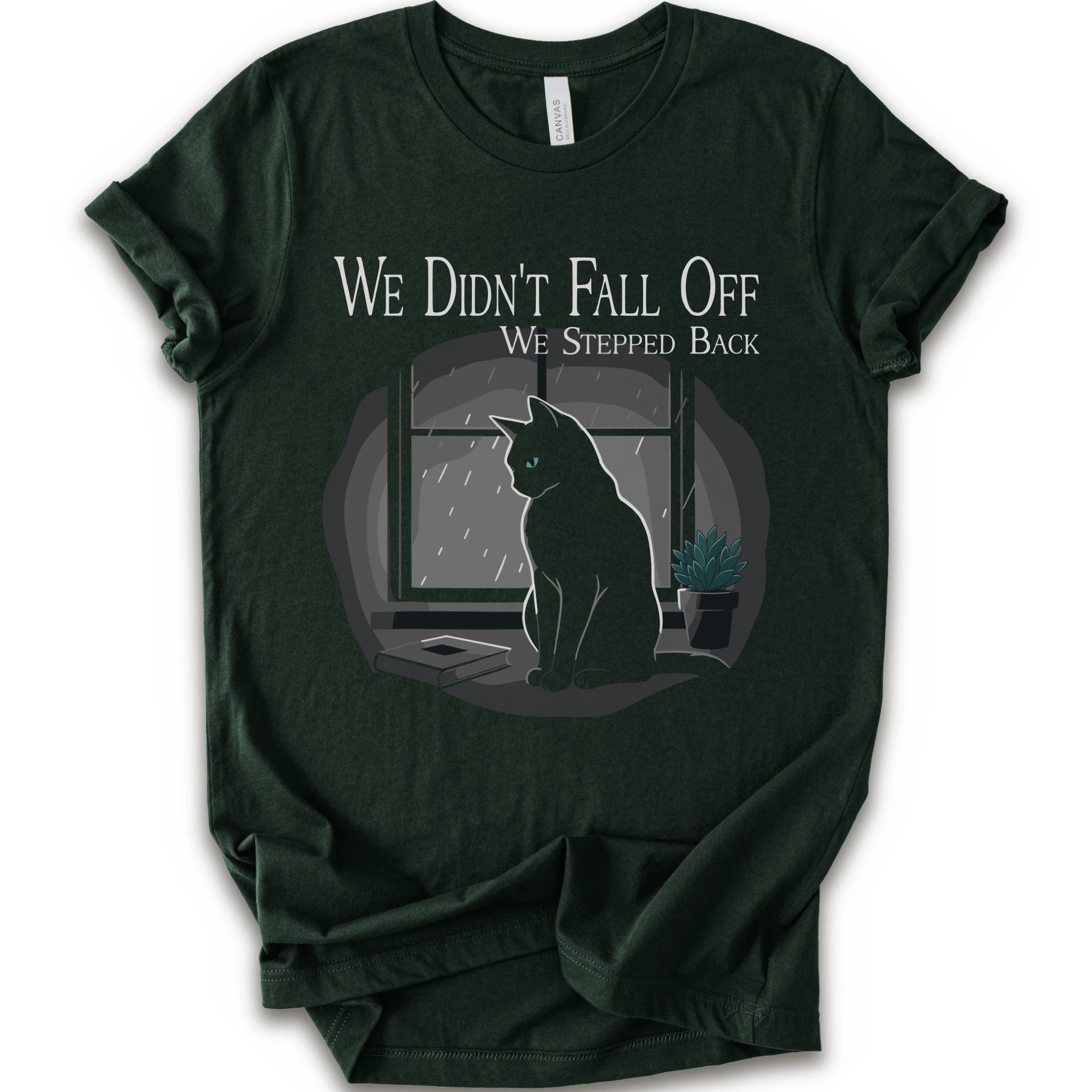 A forest short-sleeve crewneck t-shirt with a graphic print of a black cat sitting in front of a window with the text 'WE DIDN'T FALL OFF WE STEPPED BACK'.
