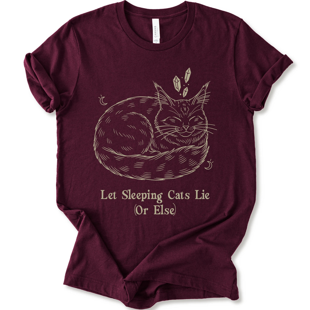 A maroon short-sleeve crewneck t-shirt with a graphic of a sleeping maine coon cat in beige line art, accompanied by the text 'Let Sleeping Cats Lie (Or Else)'.