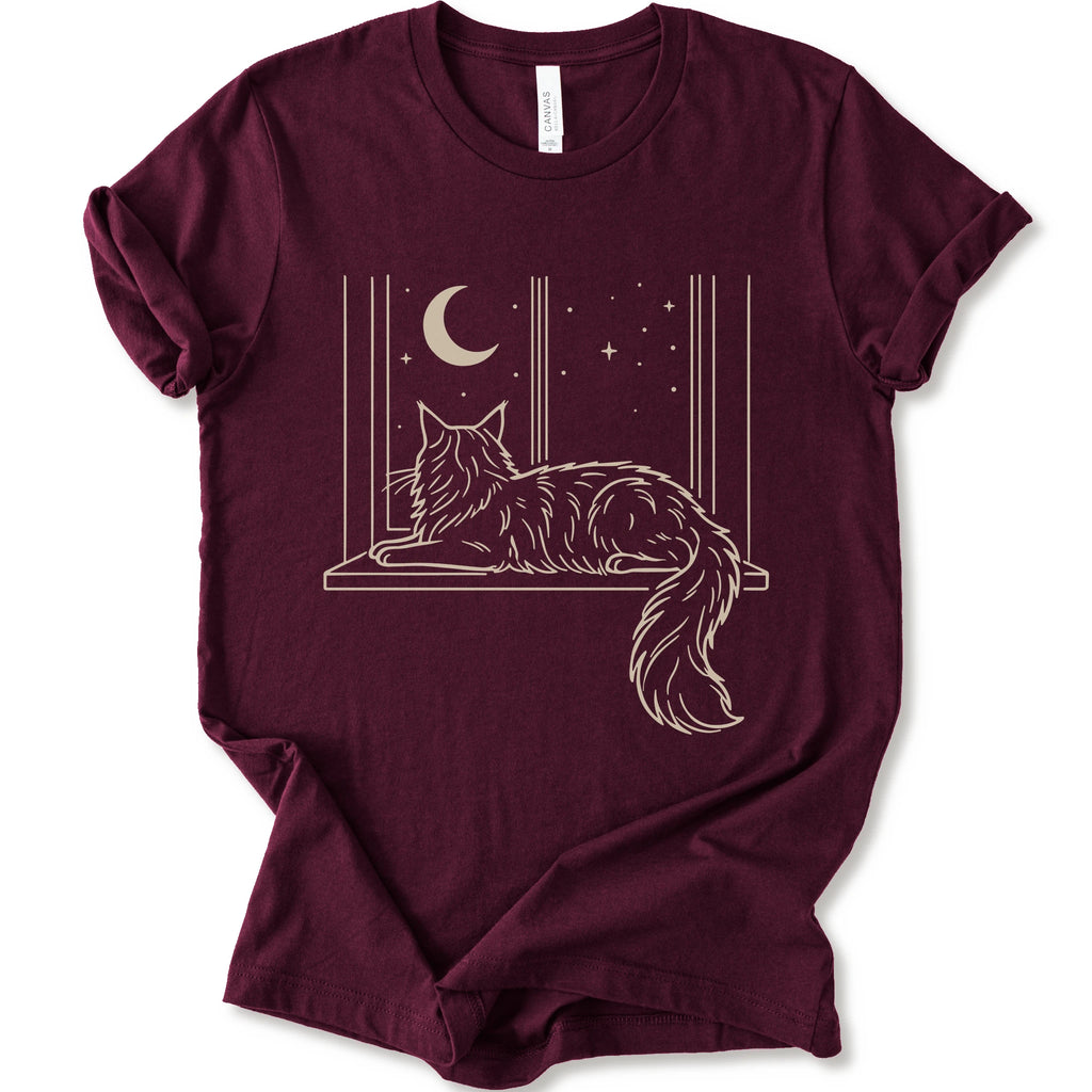 A maroon short-sleeve crewneck t-shirt with a graphic print of a long-haired maine coon resting on a windowsill under a crescent moon and stars.