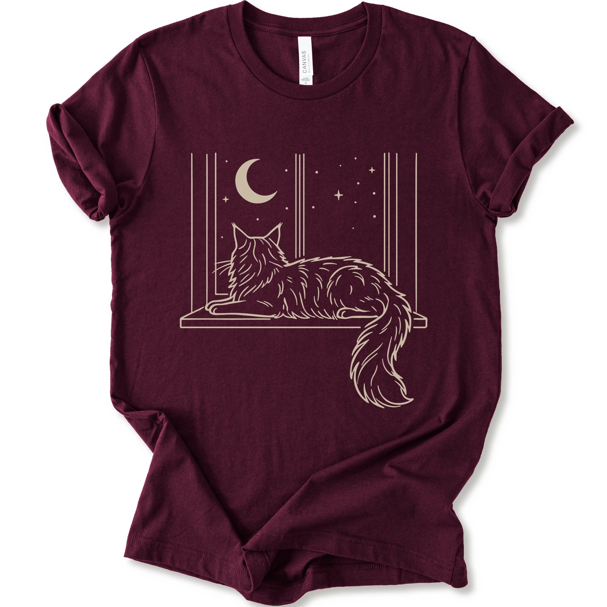 A maroon short-sleeve crewneck t-shirt with a graphic print of a long-haired maine coon resting on a windowsill under a crescent moon and stars.