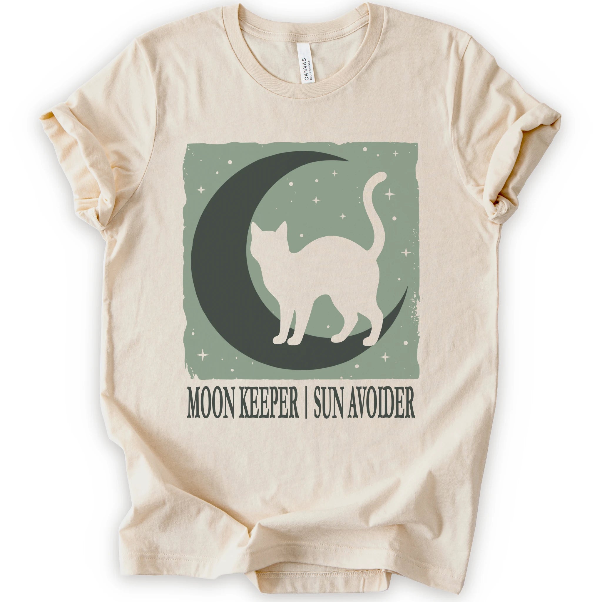 A natural short-sleeve crewneck t-shirt with a graphic print of a black cat silhouette walking on a crescent moon against a sage green starry background, with the text 'MOON KEEPER | SUN AVOIDER' printed below.