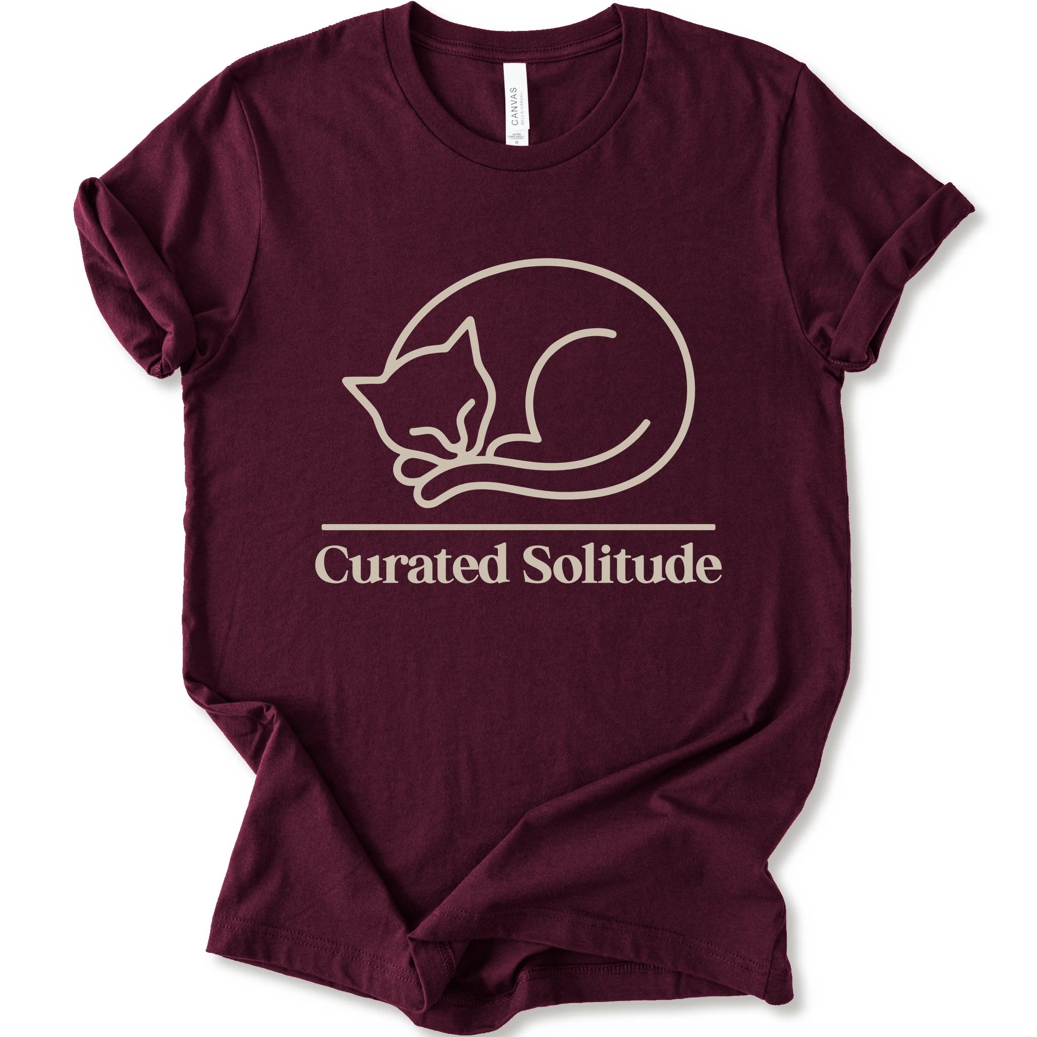 A maroon short-sleeve crewneck t-shirt with a cream-colored graphic of a curled-up sleeping cat, with the text 'Curated Solitude' printed below.
