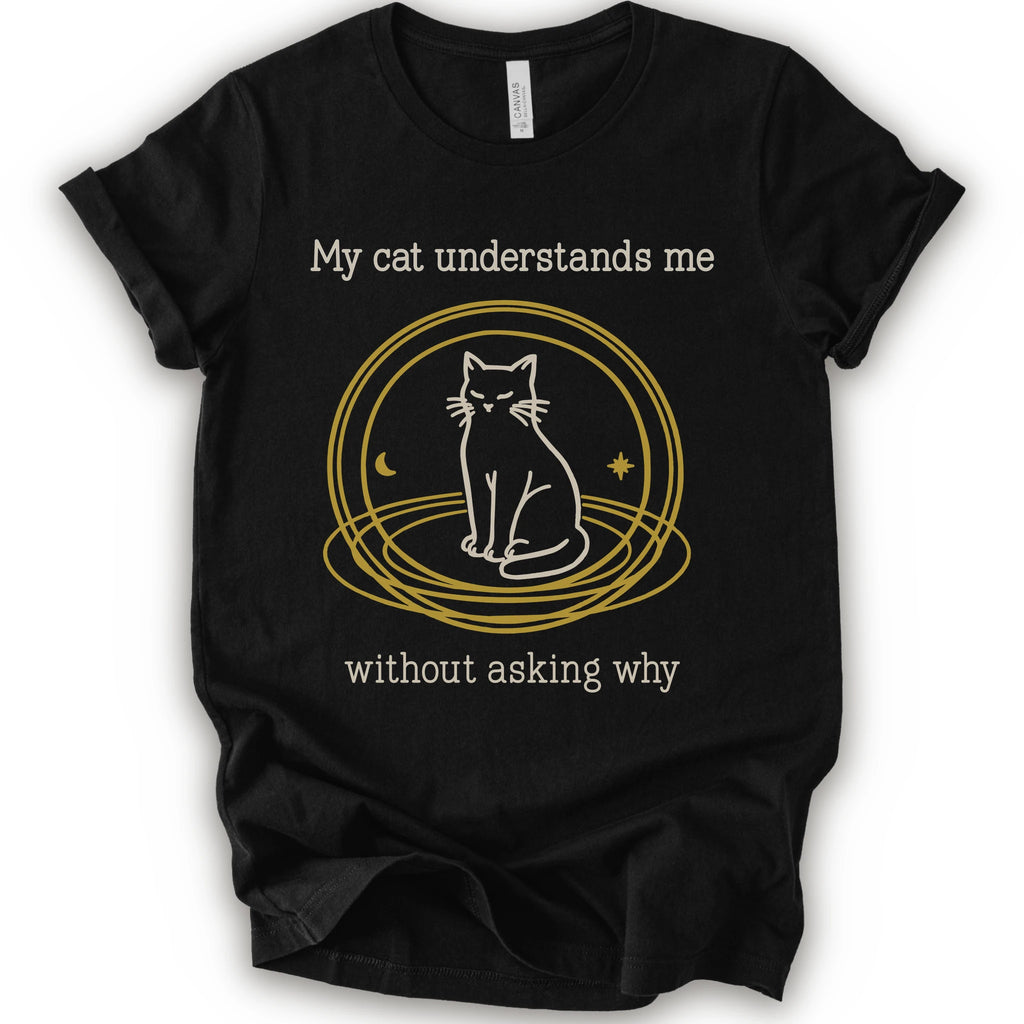 A black t-shirt with a graphic of a white cat sitting inside a gold circular frame, with the text 'My cat understands me without asking why' in a light beige font.
