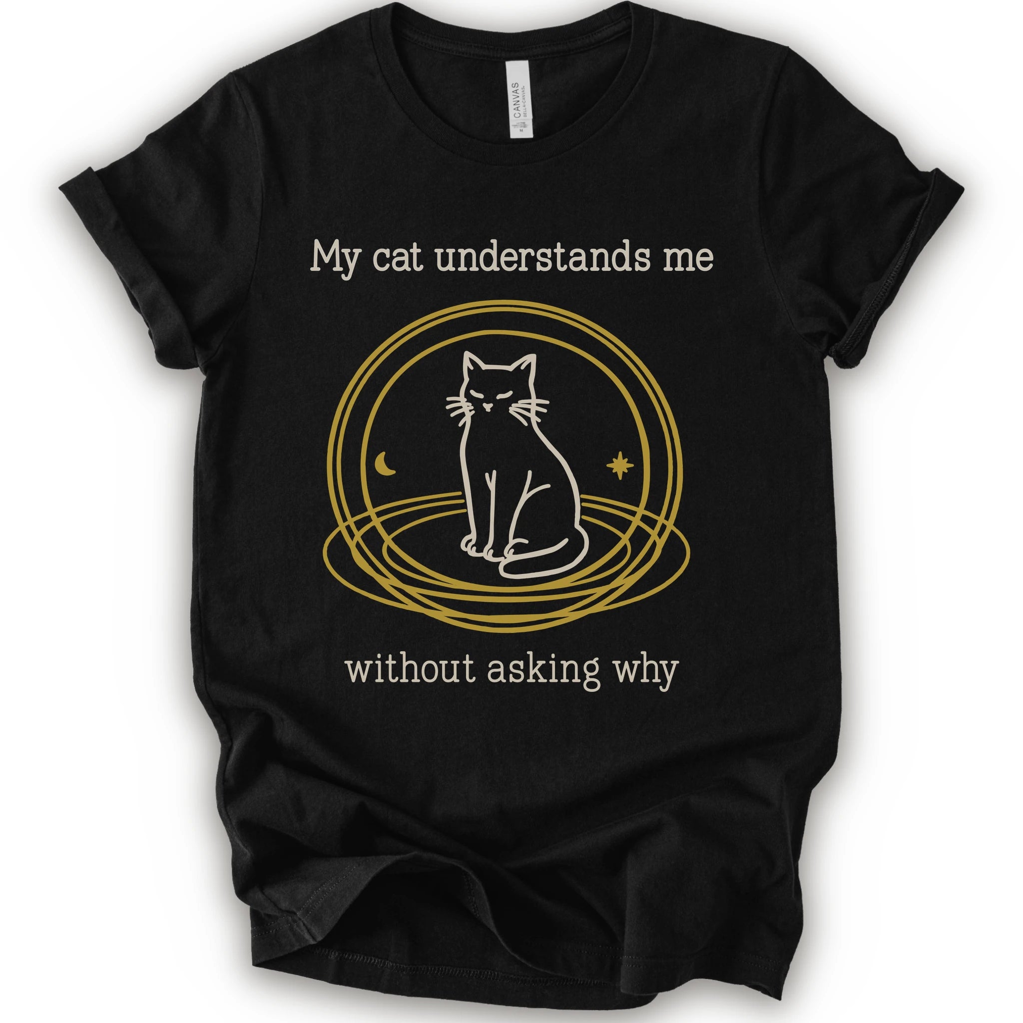 A black t-shirt with a graphic of a white cat sitting inside a gold circular frame, with the text 'My cat understands me without asking why' in a light beige font.
