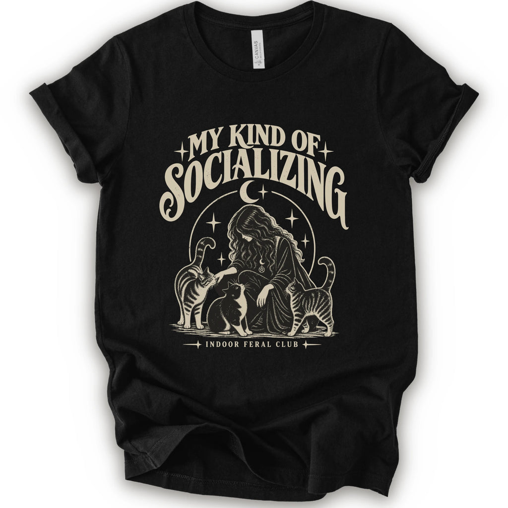 A black short-sleeve t-shirt with a cream-colored graphic print on the front. The graphic features the text 'MY KIND OF SOCIALIZING' in a stylized font above an illustration of a woman surrounded by cats under a crescent moon, with 'INDOOR FERAL CLUB' printed below.