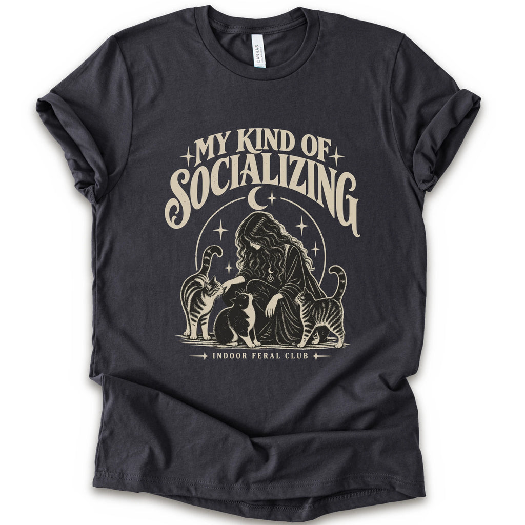 A dark grey short-sleeve t-shirt with a cream-colored graphic print on the front. The graphic features the text 'MY KIND OF SOCIALIZING' in a stylized font above an illustration of a woman surrounded by cats under a crescent moon, with 'INDOOR FERAL CLUB' printed below.