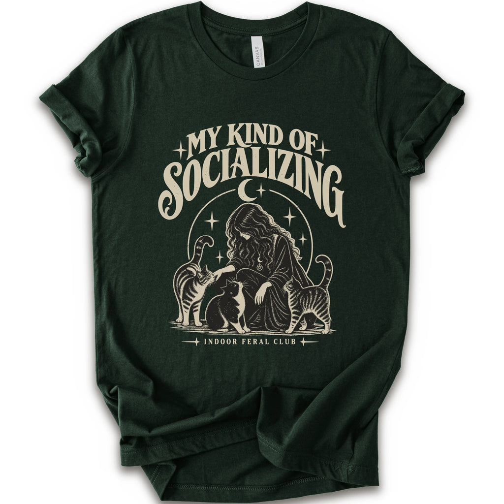 A forest short-sleeve t-shirt with a cream-colored graphic print on the front. The graphic features the text 'MY KIND OF SOCIALIZING' in a stylized font above an illustration of a woman surrounded by cats under a crescent moon, with 'INDOOR FERAL CLUB' printed below.