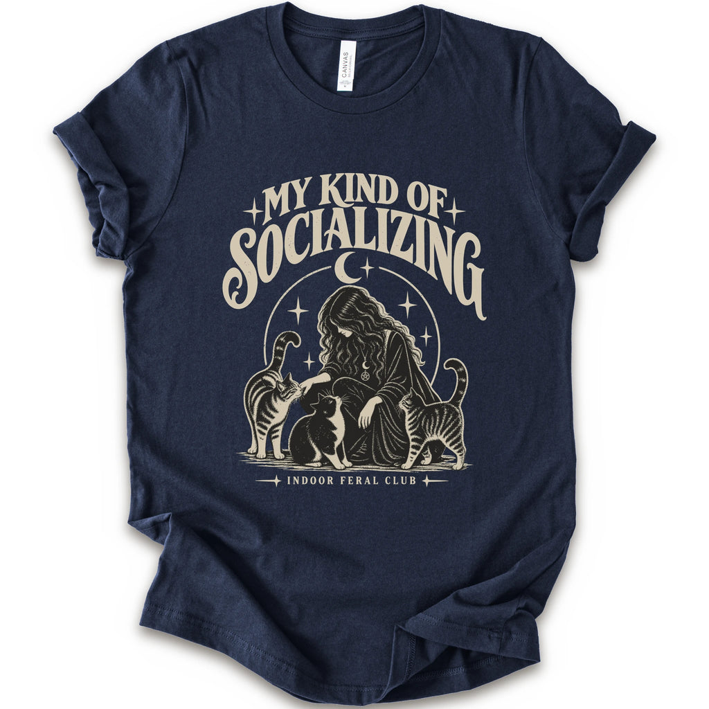 A navy short-sleeve t-shirt with a cream-colored graphic print on the front. The graphic features the text 'MY KIND OF SOCIALIZING' in a stylized font above an illustration of a woman surrounded by cats under a crescent moon, with 'INDOOR FERAL CLUB' printed below.