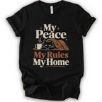 A black short-sleeve crewneck t-shirt with a retro-style graphic print that reads 'My Peace My Rules My Home' in cream and brown text, featuring an illustration of a black cat under a brown blanket next to a small mug.