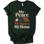A forest short-sleeve crewneck t-shirt with a retro-style graphic print that reads 'My Peace My Rules My Home' in cream and brown text, featuring an illustration of a black cat under a brown blanket next to a small mug.