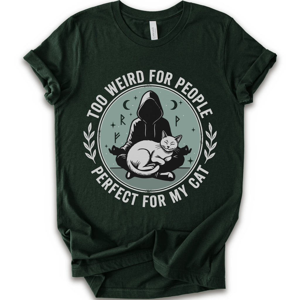 A forest short-sleeve crewneck t-shirt with a circular graphic on the front. The graphic features a dark silhouette of a person in a hood sitting cross-legged next to a white cat, surrounded by the text 'TOO WEIRD FOR PEOPLE' on top and 'PERFECT FOR MY CAT' on the bottom, with small moon and star details.