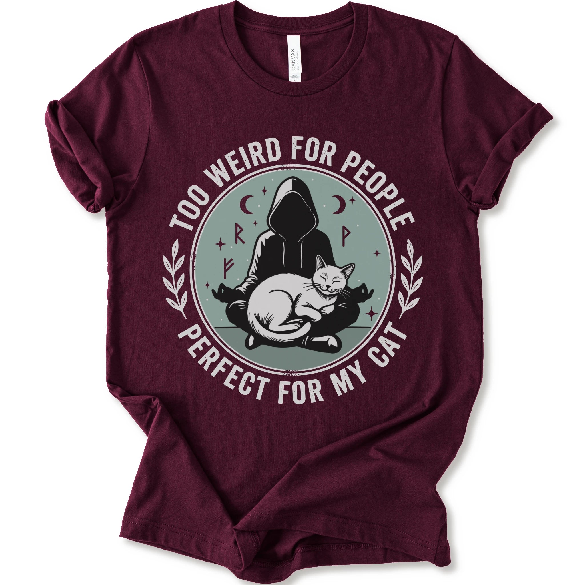 A maroon short-sleeve crewneck t-shirt with a circular graphic on the front. The graphic features a dark silhouette of a person in a hood sitting cross-legged next to a white cat, surrounded by the text 'TOO WEIRD FOR PEOPLE' on top and 'PERFECT FOR MY CAT' on the bottom, with small moon and star details.