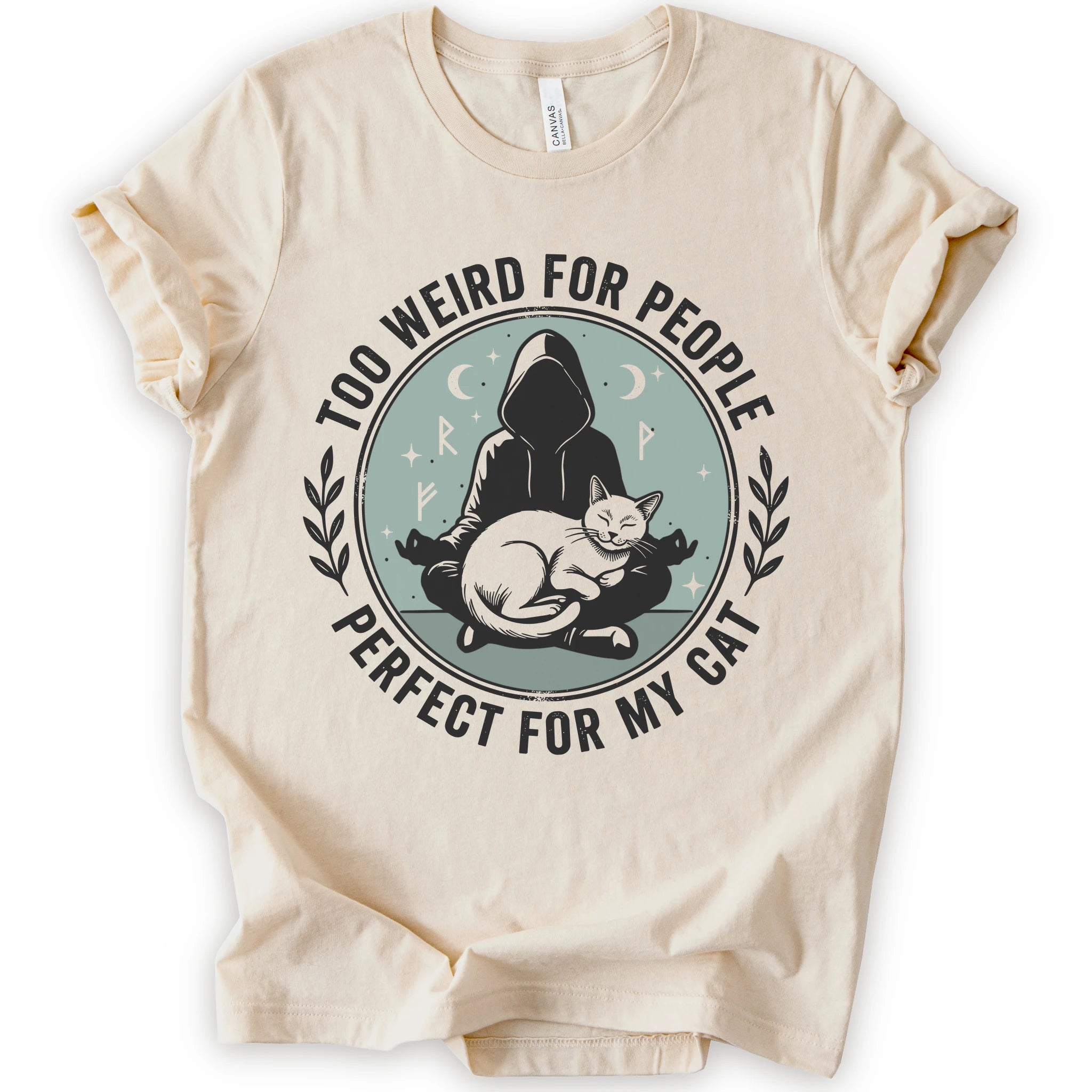 A natural short-sleeve crewneck t-shirt with a circular graphic on the front. The graphic features a dark silhouette of a person in a hood sitting cross-legged next to a white cat, surrounded by the text 'TOO WEIRD FOR PEOPLE' on top and 'PERFECT FOR MY CAT' on the bottom, with small moon and star details.