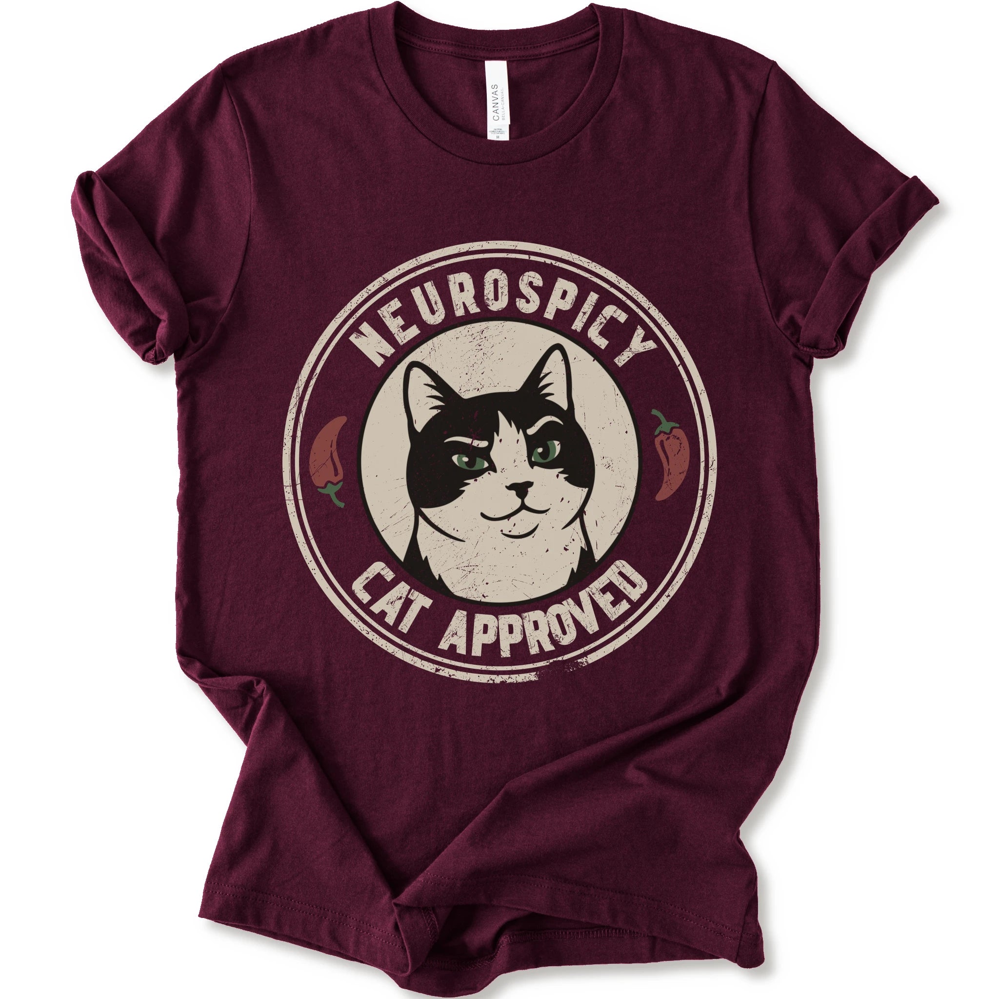A maroon short-sleeve crewneck t-shirt with a distressed circular graphic on the chest featuring a black and white cat with green eyes, red peppers, and the text 'NEUROSPICY, CAT APPROVED'.