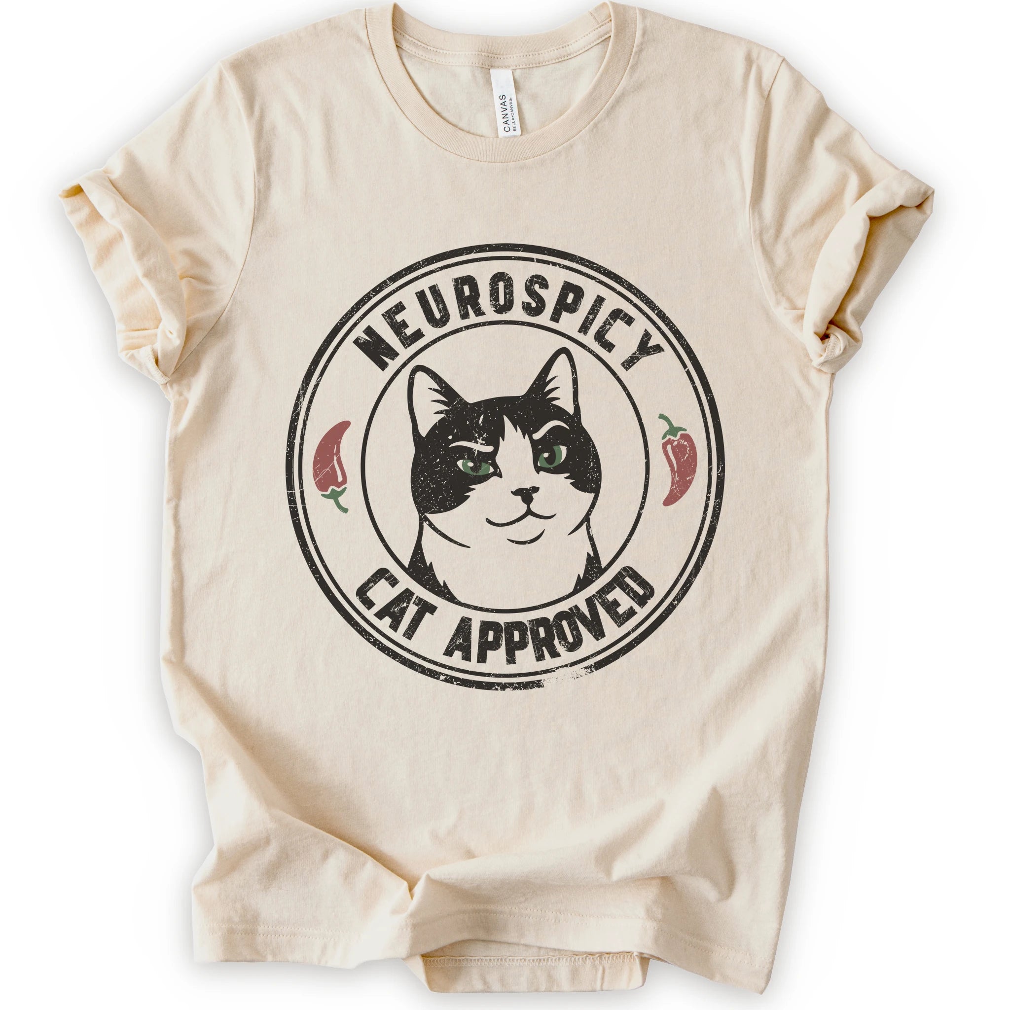 A natural short-sleeve crewneck t-shirt with a distressed circular graphic on the chest featuring a black and white cat with green eyes, red peppers, and the text 'NEUROSPICY, CAT APPROVED'.