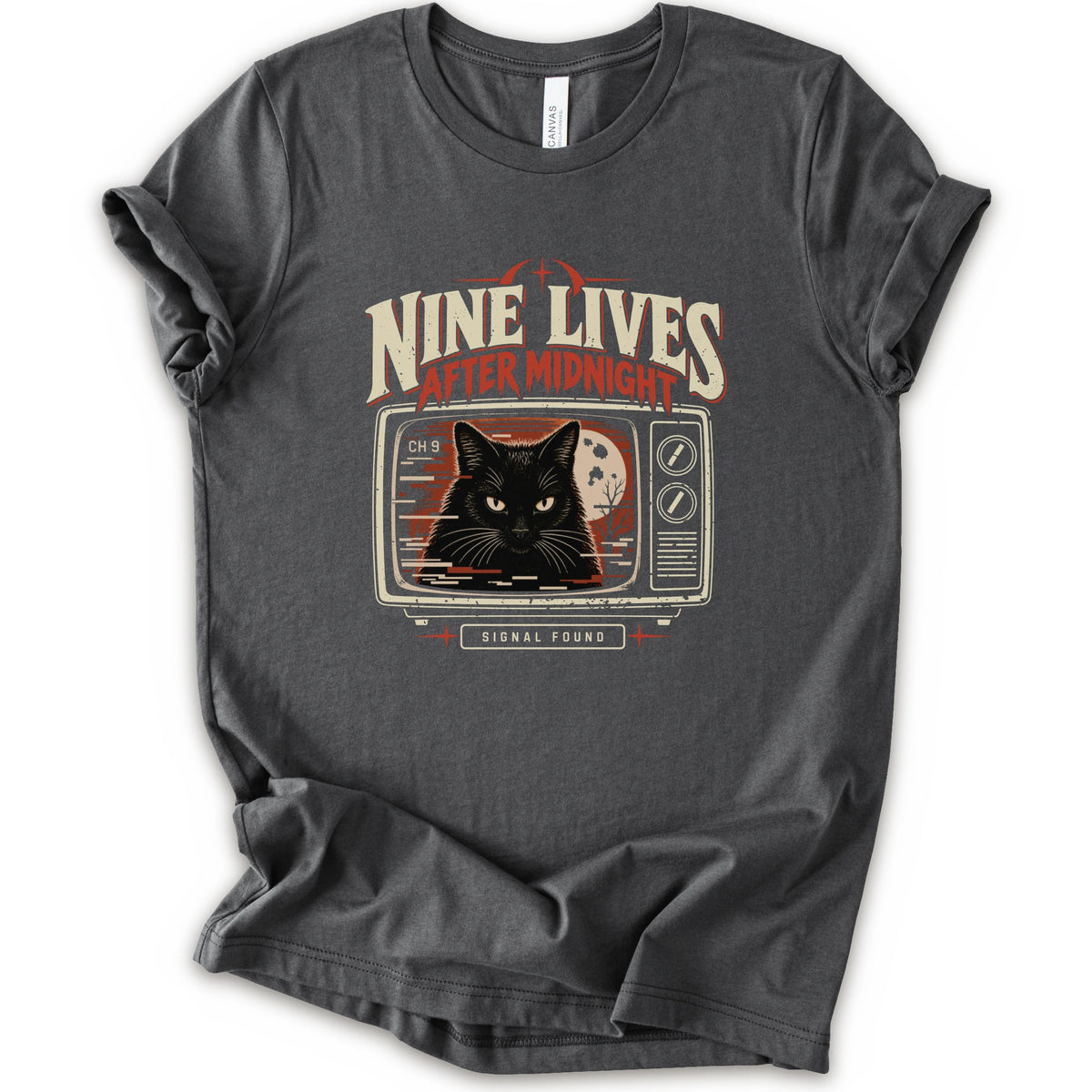 An asphalt short-sleeve crewneck t-shirt with a vintage-style graphic on the front. The graphic features the text 'NINE LIVES AFTER MIDNIGHT' in distressed cream and red lettering above an illustration of a black cat's face on a retro television screen, with 'SIGNAL FOUND' written below.