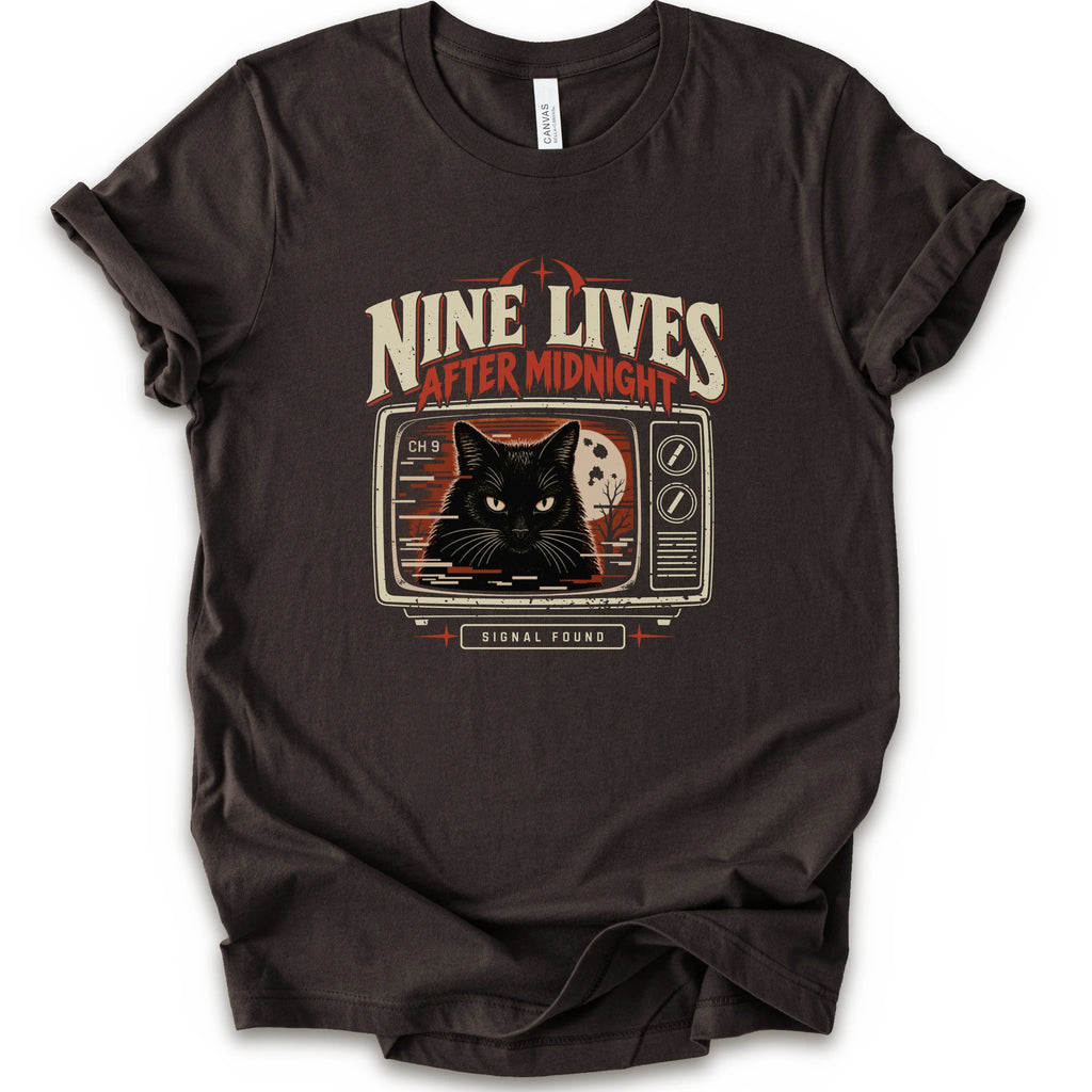 A brown short-sleeve crewneck t-shirt with a vintage-style graphic on the front. The graphic features the text 'NINE LIVES AFTER MIDNIGHT' in distressed cream and red lettering above an illustration of a black cat's face on a retro television screen, with 'SIGNAL FOUND' written below.