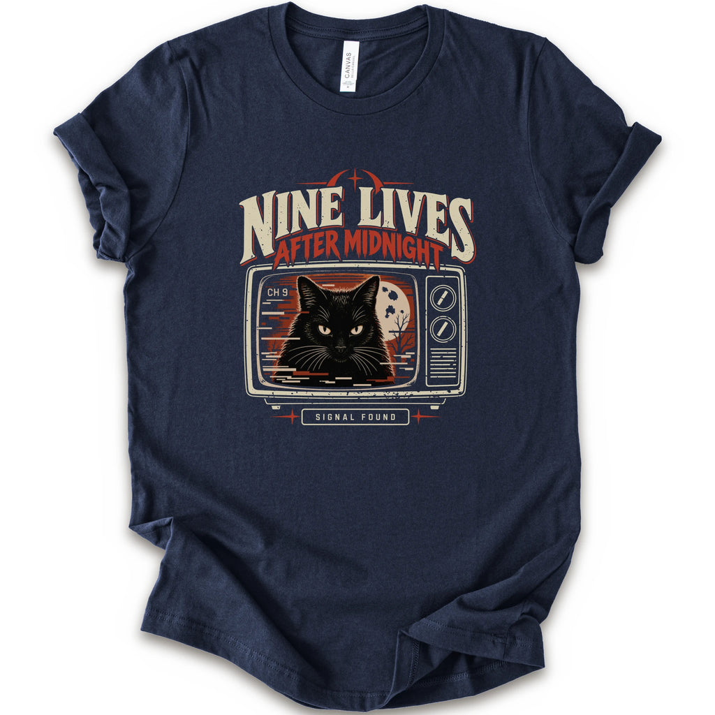 A navy short-sleeve crewneck t-shirt with a vintage-style graphic on the front. The graphic features the text 'NINE LIVES AFTER MIDNIGHT' in distressed cream and red lettering above an illustration of a black cat's face on a retro television screen, with 'SIGNAL FOUND' written below.