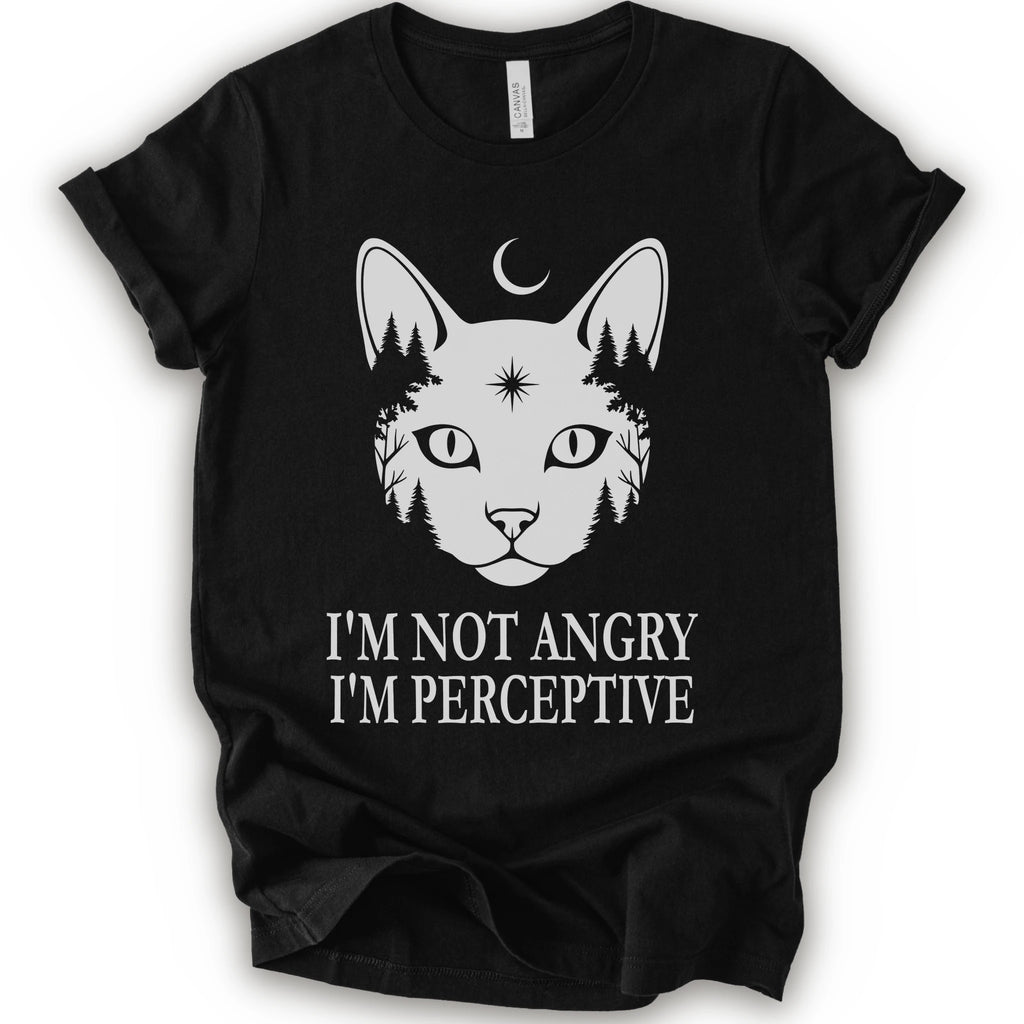 A black short-sleeve crewneck t-shirt with a white graphic of a cat's face containing pine trees and a crescent moon, with the text 'I'M NOT ANGRY I'M PERCEPTIVE' printed below.