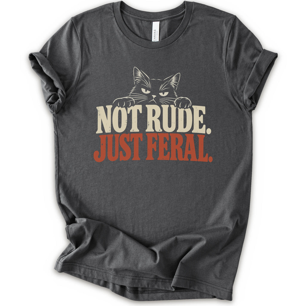 An asphalt short-sleeve t-shirt with a graphic print of a cat with narrowed eyes and visible paws peers over the words “NOT RUDE.” above a large rust-colored “JUST FERAL.” The design uses bold distressed serif lettering in cream and rust with a retro graphic look.