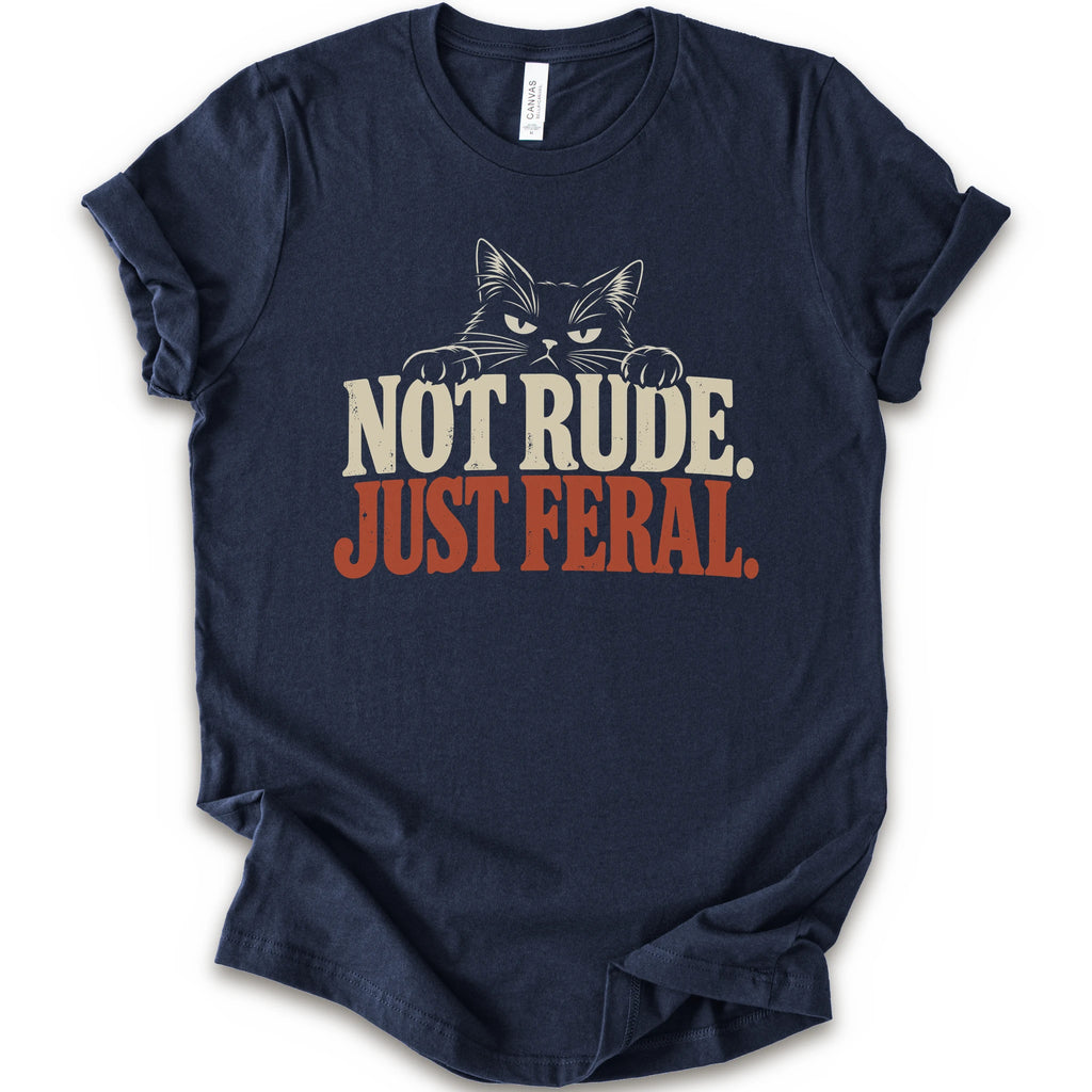 A navy short-sleeve t-shirt with a graphic print of a cat with narrowed eyes and visible paws peers over the words “NOT RUDE.” above a large rust-colored “JUST FERAL.” The design uses bold distressed serif lettering in cream and rust with a retro graphic look.
