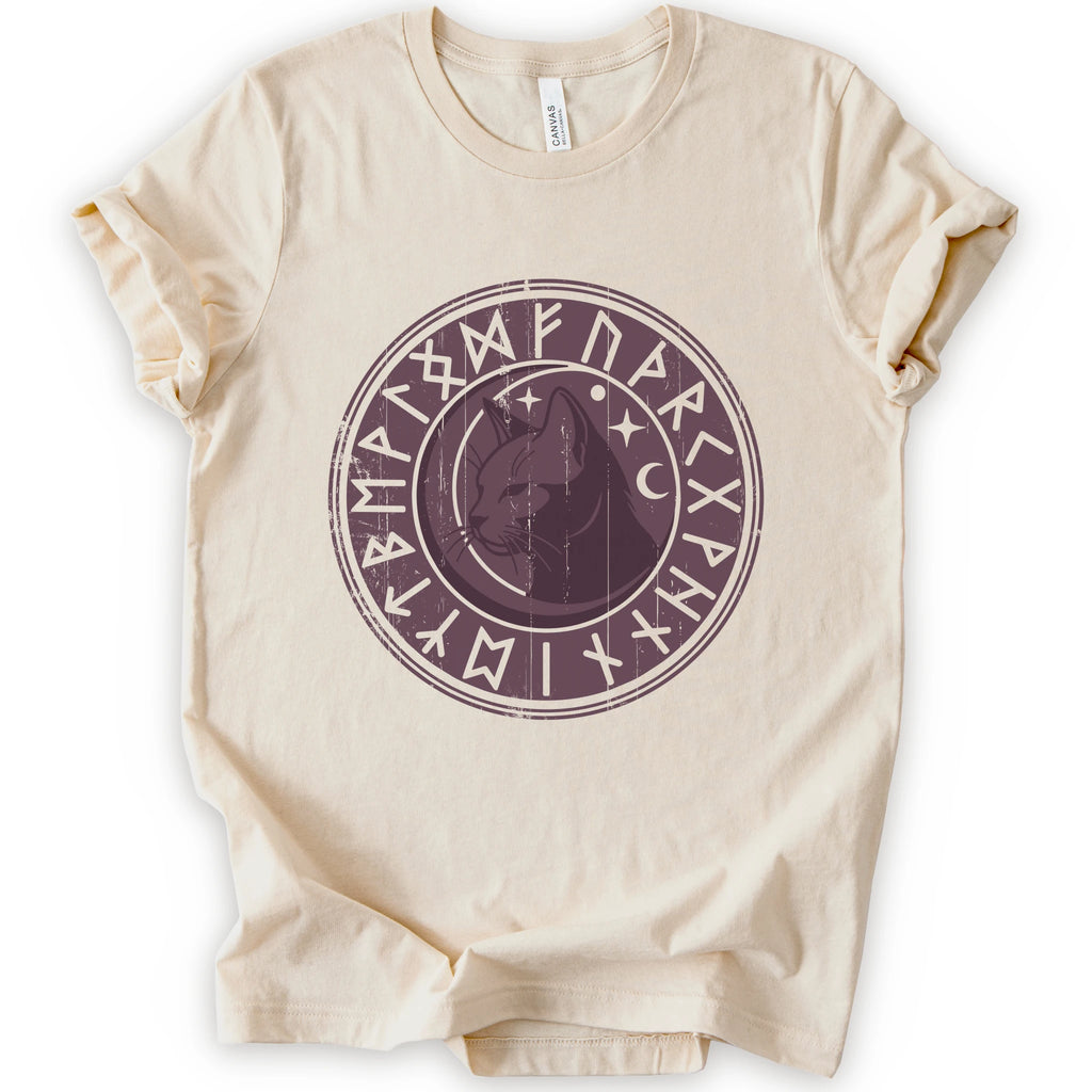 A natural short-sleeve crewneck t-shirt with a circular dark purple graphic on the chest featuring a cat's face surrounded by runic symbols.