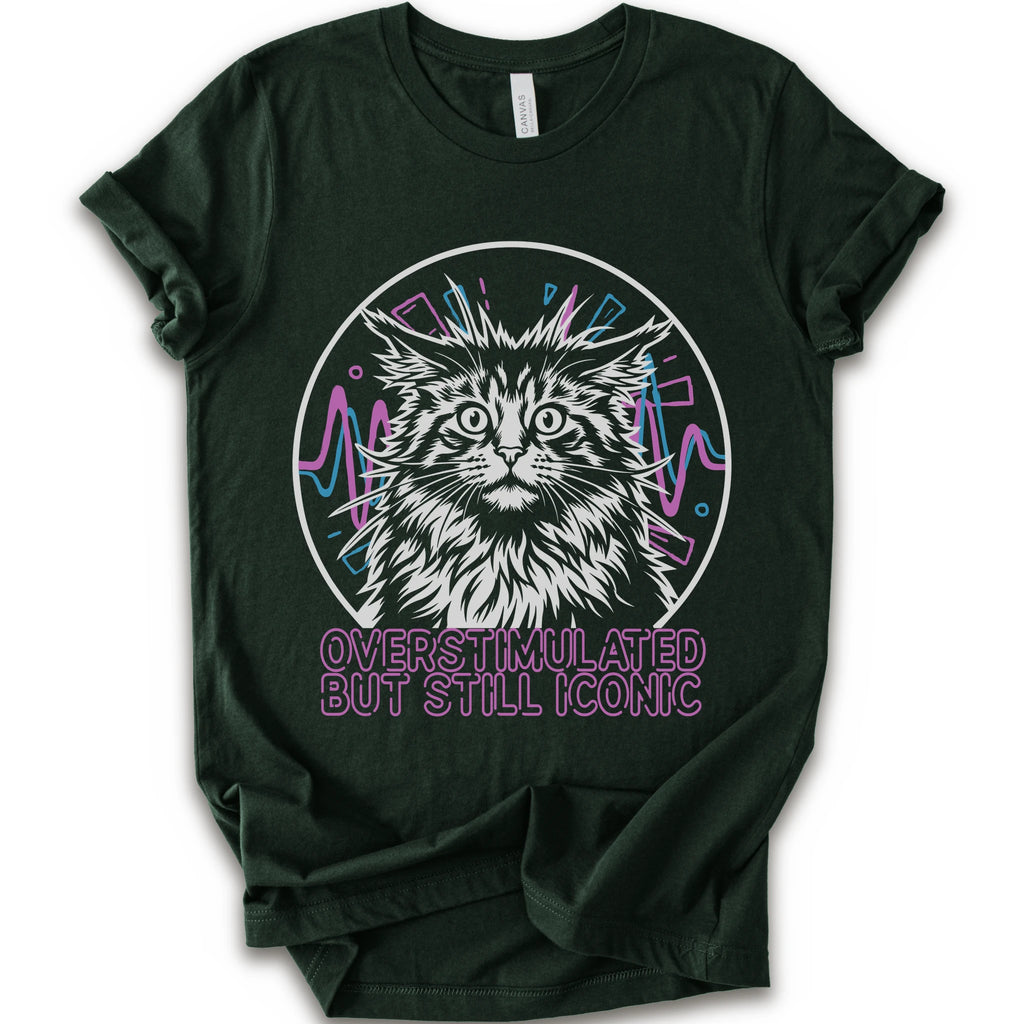 A forest short-sleeve crewneck t-shirt featuring a graphic of a white and gray maine con cat inside a circular frame with pink and blue accents, and the text 'OVERSTIMULATED BUT STILL ICONIC' in pink below.