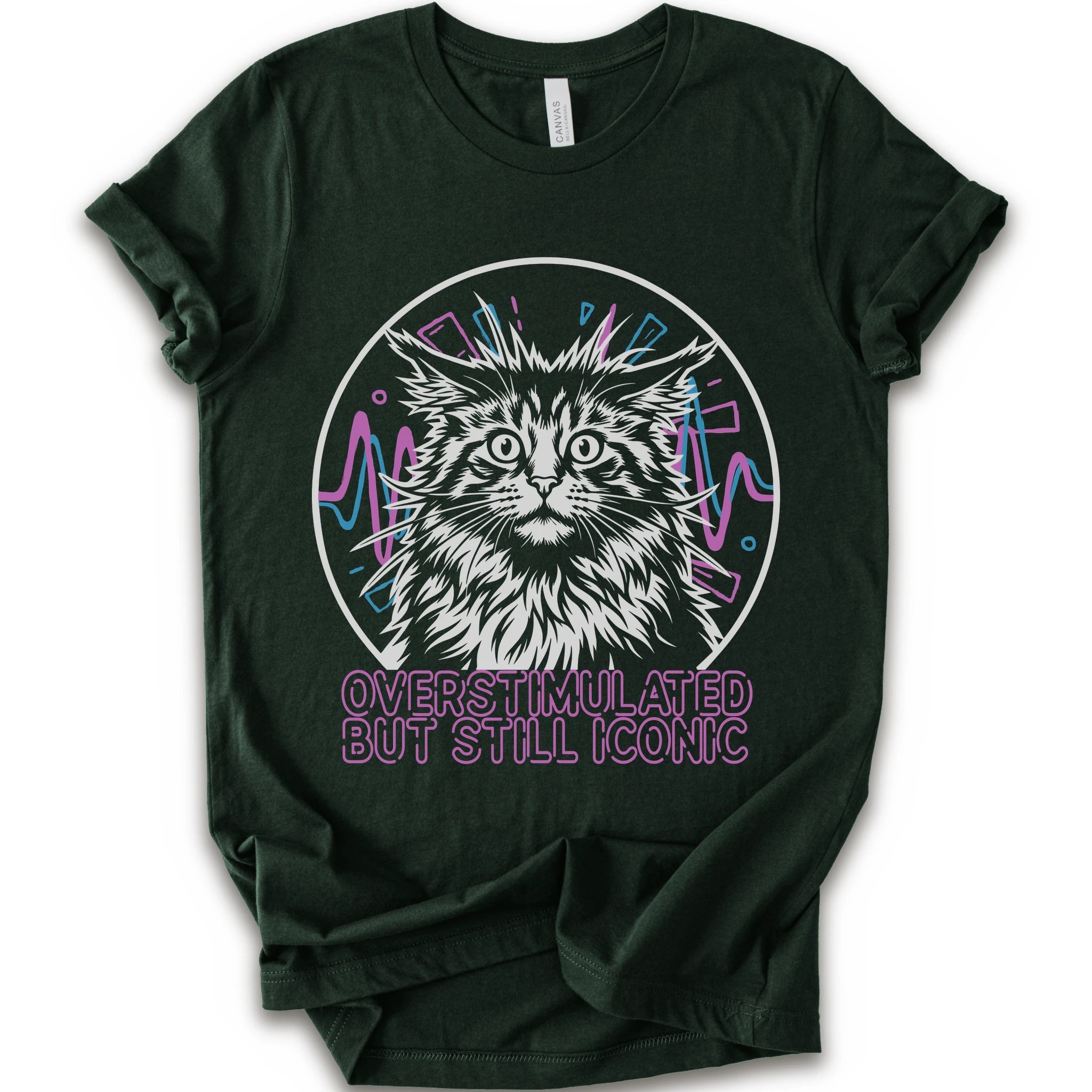 A forest short-sleeve crewneck t-shirt featuring a graphic of a white and gray maine con cat inside a circular frame with pink and blue accents, and the text 'OVERSTIMULATED BUT STILL ICONIC' in pink below.