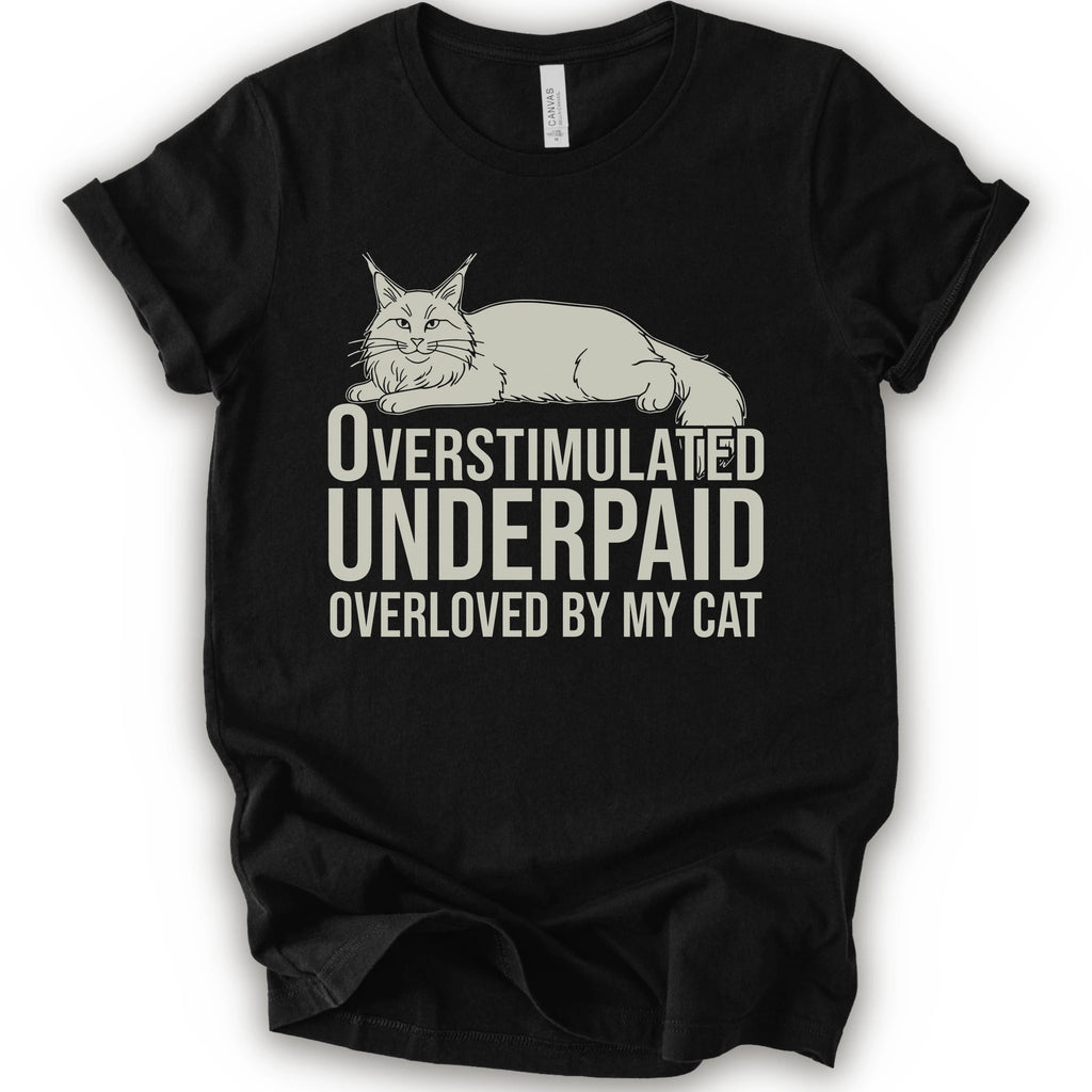 A black short-sleeve crewneck T-shirt with a lounging cat graphic and “Overstimulated, Underpaid, Overloved by My Cat” text.